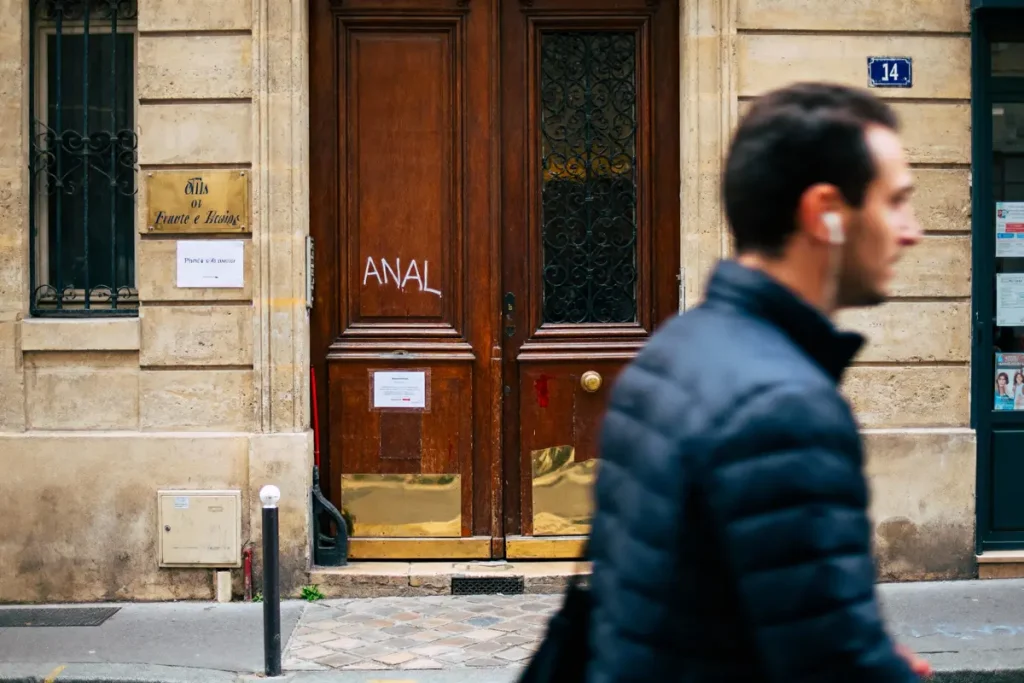 Homme flou passant devant une porte en bois avec graffiti sur bâtiment ancien. Numéro 14 visible.
