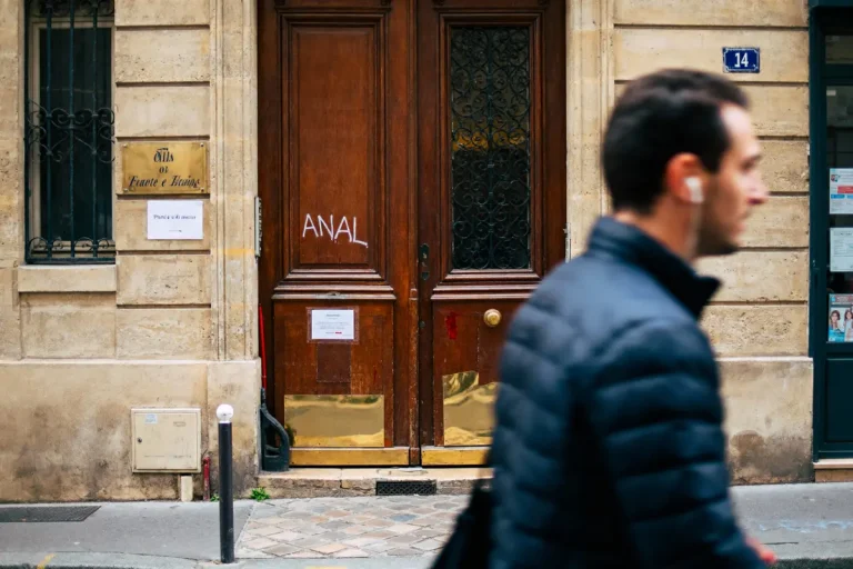 Homme flou passant devant une porte en bois avec graffiti sur bâtiment ancien. Numéro 14 visible.