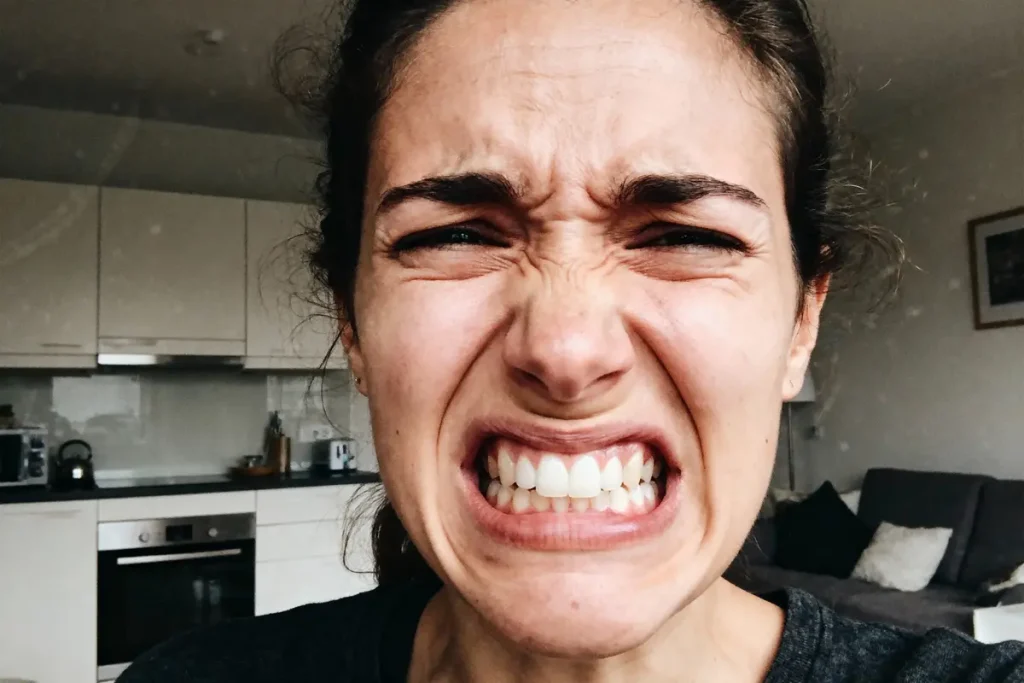 Personne exprimant une intense émotion, visage crispé, sourcils froncés, dents serrées, dans une cuisine moderne.