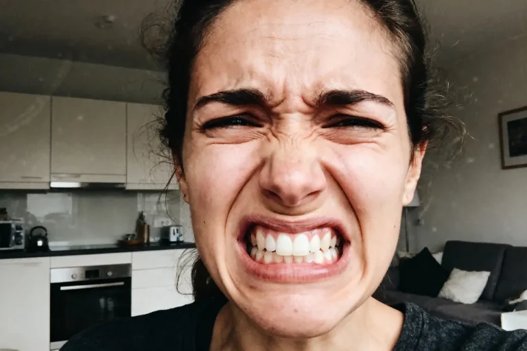 Personne exprimant une intense émotion, visage crispé, sourcils froncés, dents serrées, dans une cuisine moderne.