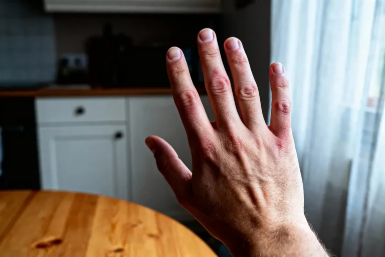 Une main tendue dans une cuisine, table en bois et fenêtre avec rideaux en arrière-plan.