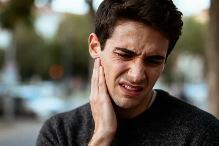 Homme ressentant de la douleur à l'oreille, main sur la joue, expression faciale de gêne ou mal-être.
