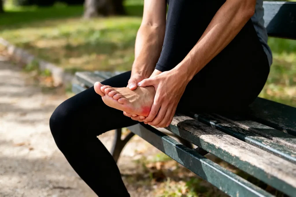 Personne assise sur un banc, tenant un pied douloureux en plein air.