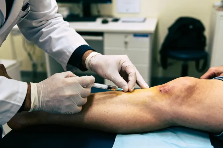 Médecin injectant une seringue dans le genou d'un patient allongé sur une table médicale.