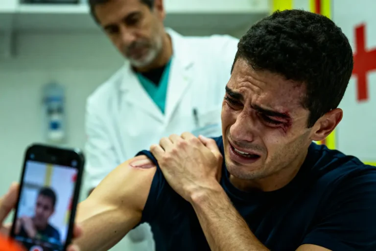 Homme blessé, en pleurs, dans une clinique, examiné par un médecin, blessure à l'épaule.