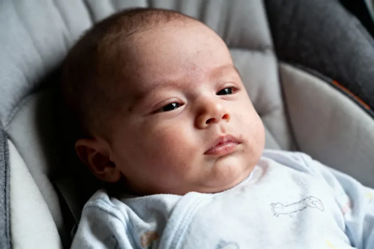 Bébé allongé dans un siège, regard pensif, habillé en pyjama clair.