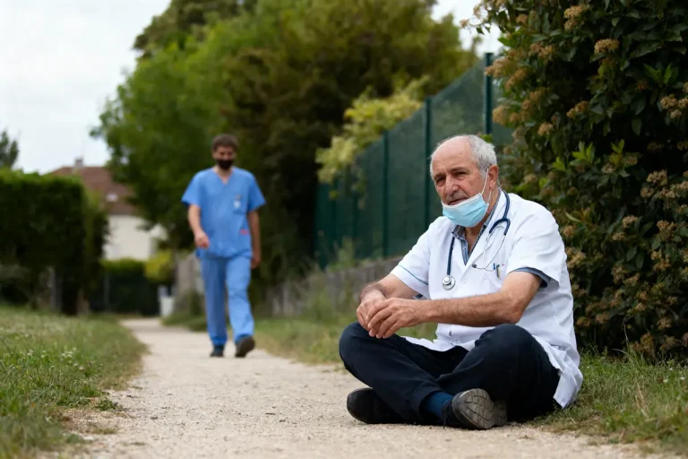 Deux professionnels de santé assis et debout sur un chemin, portants blouses médicales et masques.