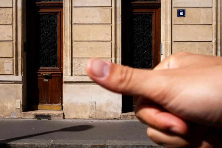 Pouce levé devant une porte en bois ornée de fer forgé sur façade en pierre.