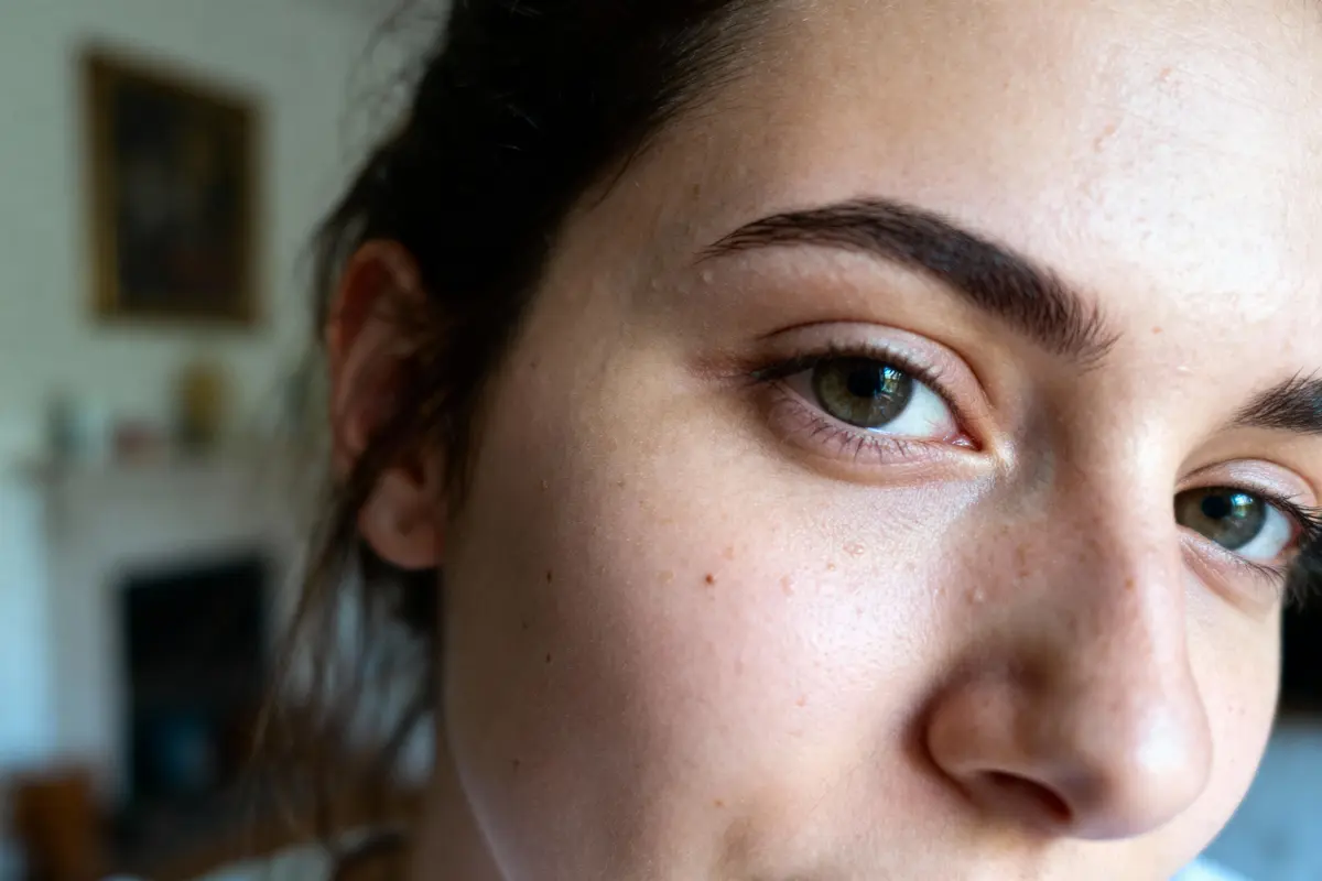 Gros plan sur le visage d'une personne, mettant en avant un œil vert et sourcil épais.