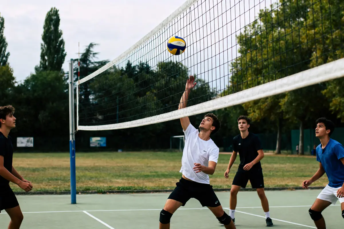 Quatre jeunes hommes jouent au volley-ball en extérieur, un sautant pour toucher le ballon.