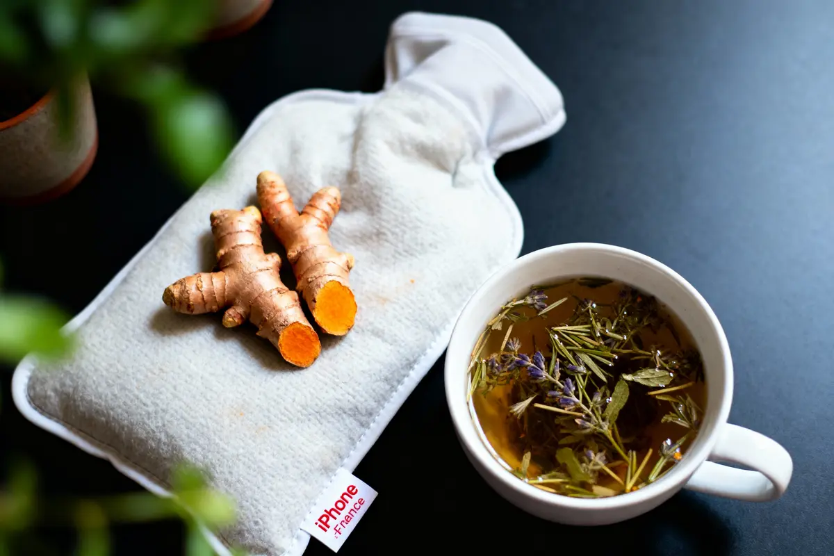 Tranches de curcuma sur bouillotte, tasse d'infusion d'herbes. Accessoires sur fond noir.