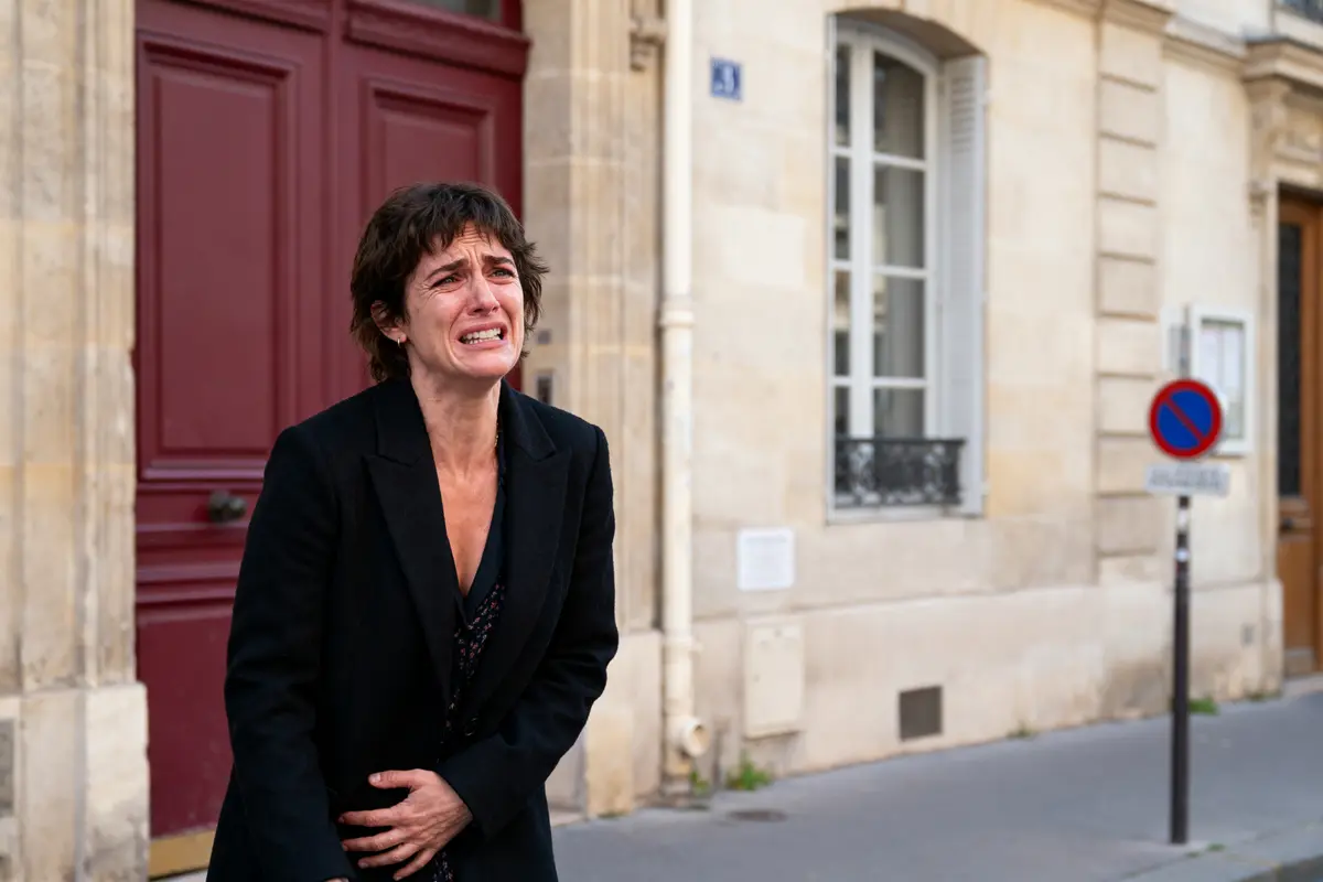 pexels-michal-pech-213601-757318 (1) Femme pleurant devant une porte rouge, habillée en noir, dans une rue. Panneau d'interdiction stationner visible.