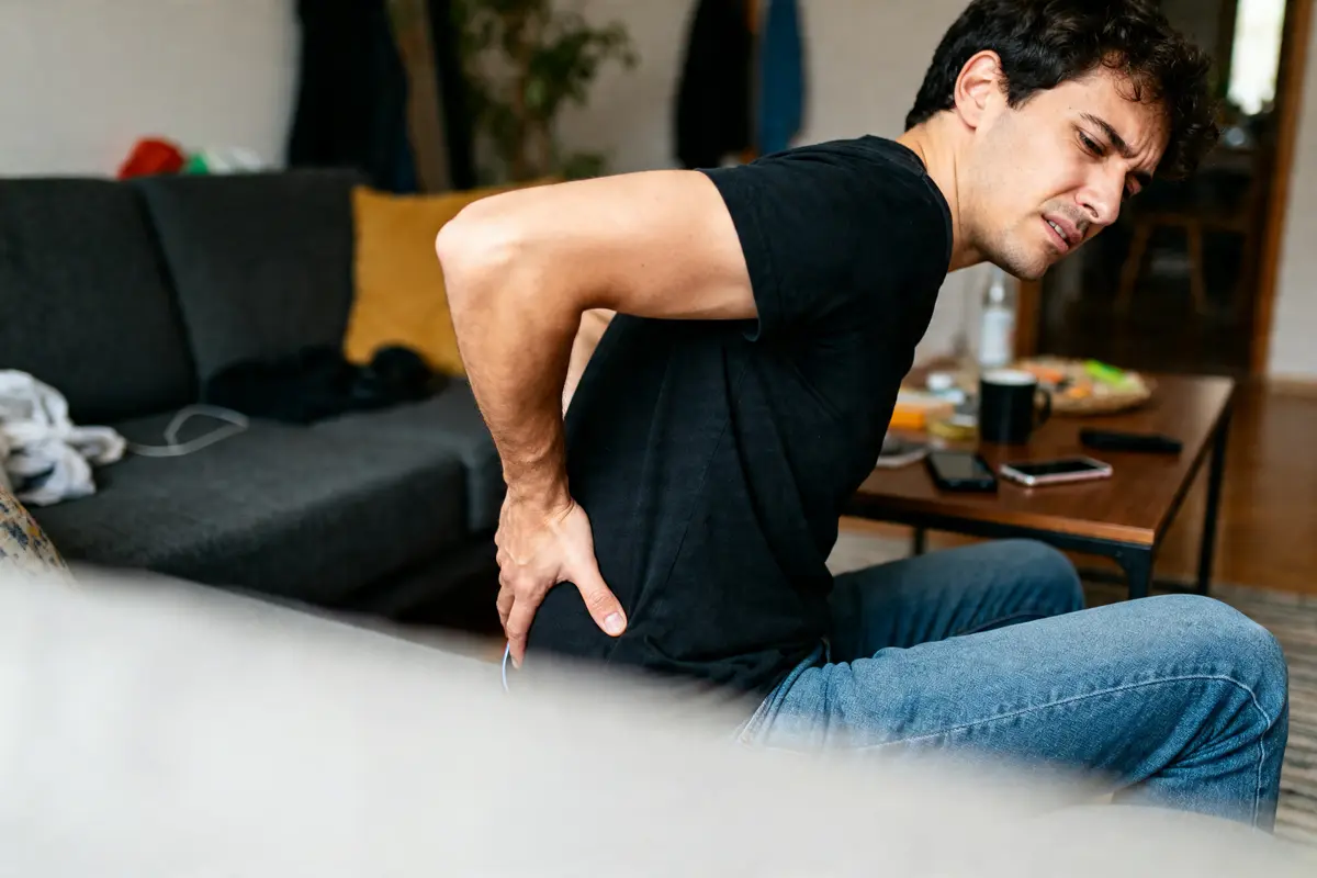 Homme assis souffrant douleur au dos, se demande combien de temps dure une douleur au coccyx