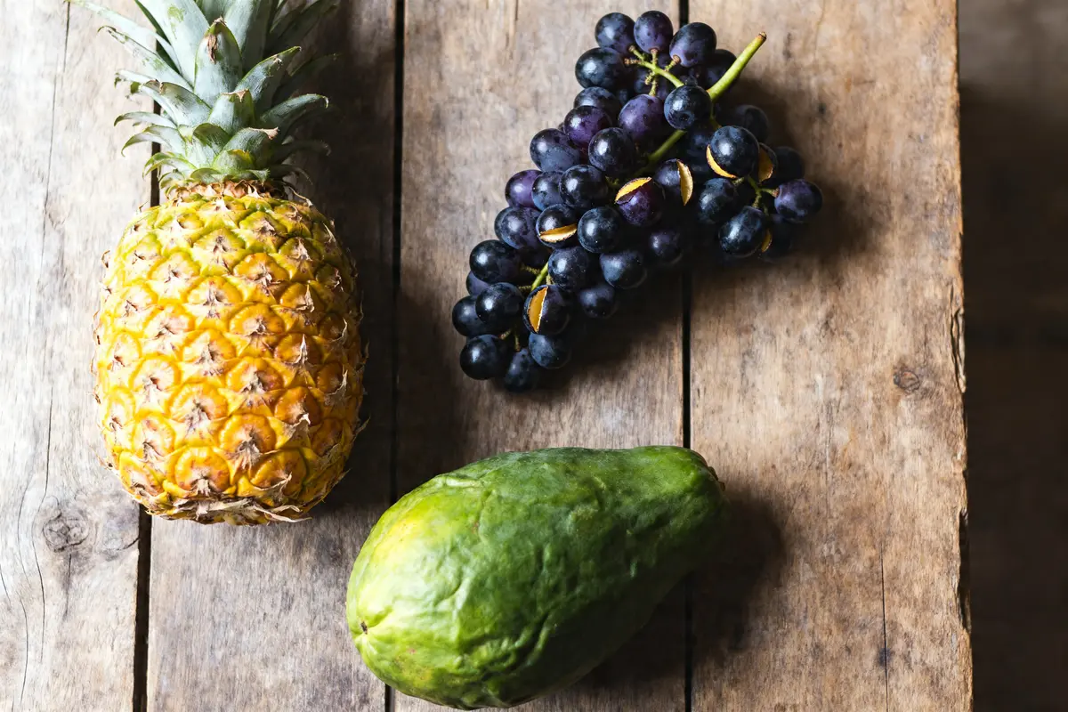 Ananas, papaye et raisins sur une table en bois les 3 fruits à éviter pendant la grossesse