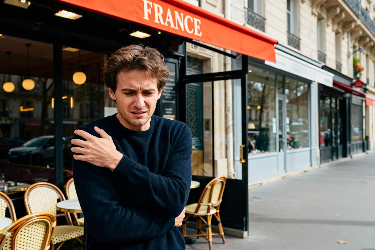 Homme souffrant de douleur à l'épaule gauche devant un café à Paris