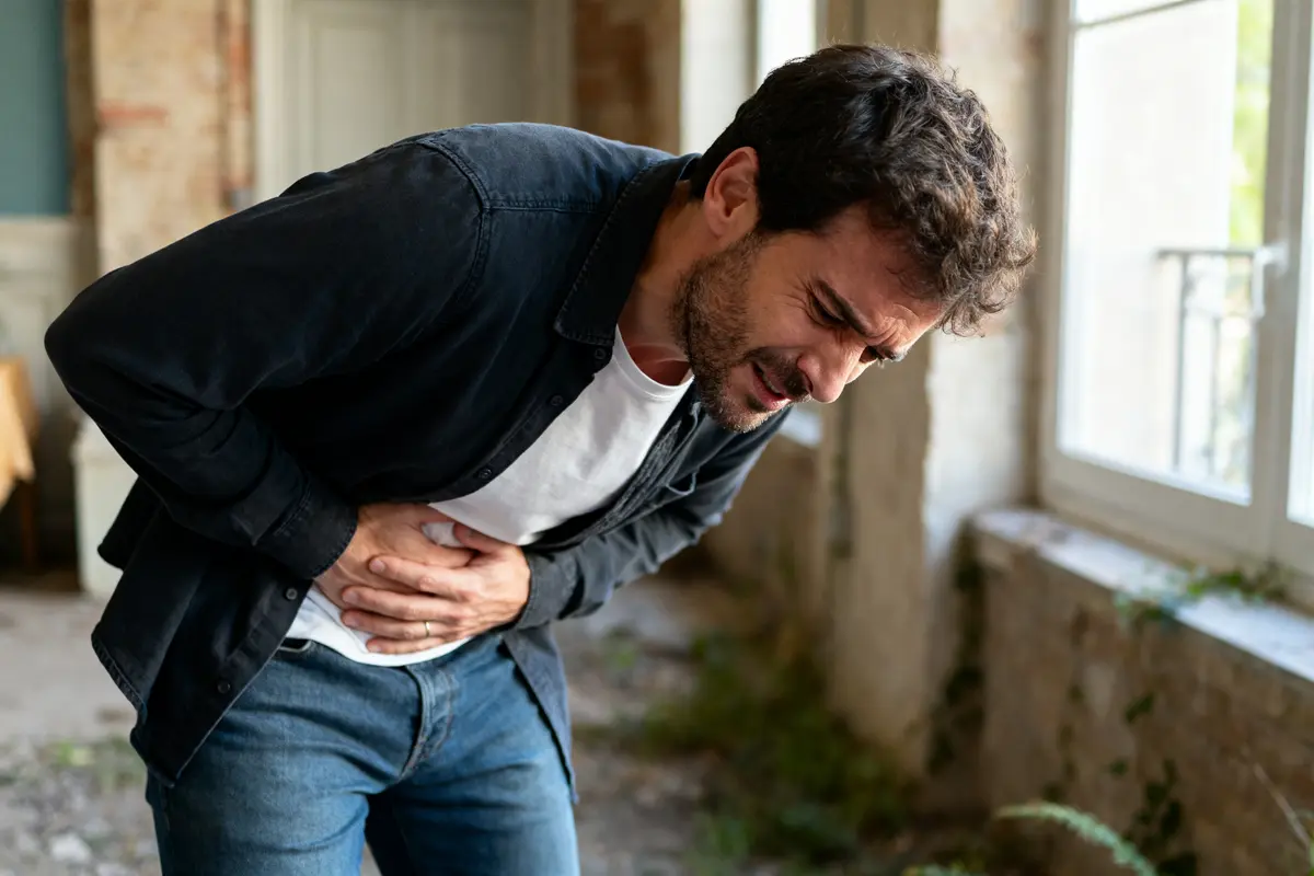 pexels-michal-pech-213601-757318 (1) Homme souffrant de douleur à l'estomac et au dos, tenant son ventre dans une pièce.